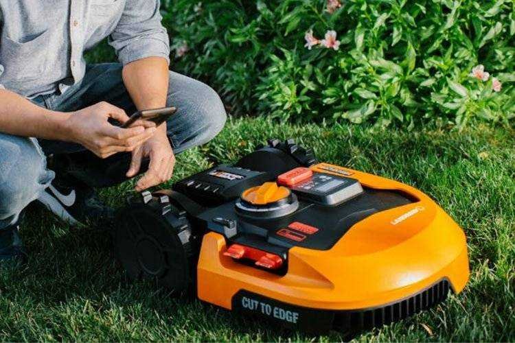 Male kneeling over Robotic Lawn Mowers